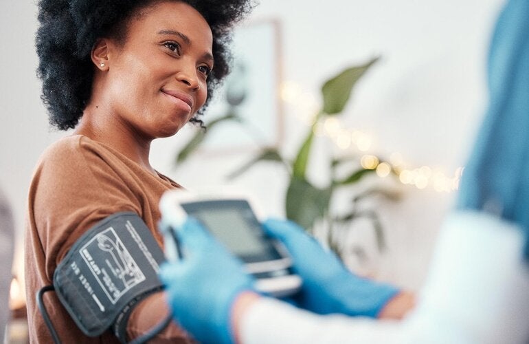 Healthcare personnel are taking the blood pressure of a young African-American woman using an automatic device.