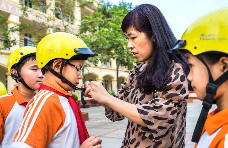 Female adult buckles helmet onto boy's head