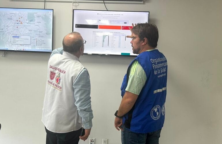 PAHO and MoH staff in front of a screen showing a dashboard