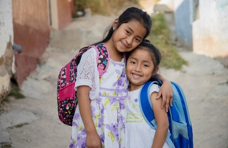 two girls standing together in a hug with their backpacks