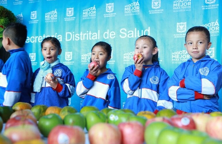 Niños y niñas vestidos con uniforme escolar deportivo, comiendo unas manzanas