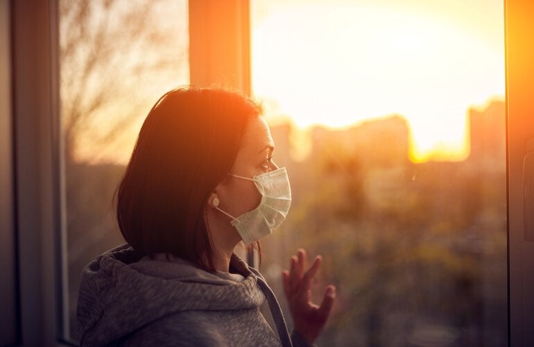 Woman with mask looking out the window at sunset