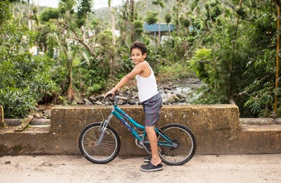 niño montando su bicicleta con árboles en el fondo