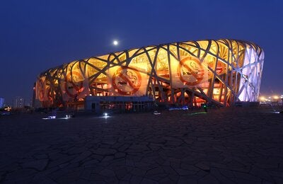 Photo of a big building shaped as a elipse, with no walls, shape made of the bent beams. In the exterior, four large banners with the icon of prohibited smoking