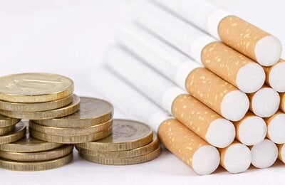 Fotografía de unas monedas apiladas junto a un grupo de cigarrillos amontonados en pirámide