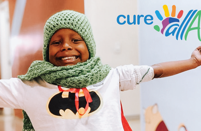 Young boy with a batman t-shirt and a wool green hat and scarf, with his arms opened and a big smile