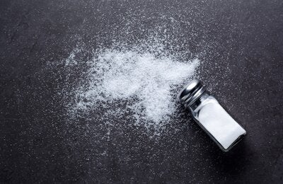 Salt shaker with salt spilt around on a dark background