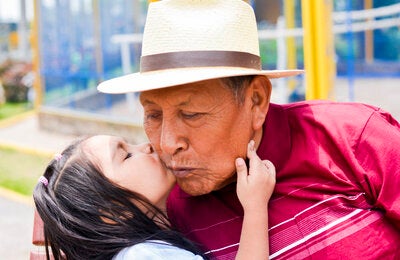 Image of an elder man with his granddaughter giving him a kiss on the cheek