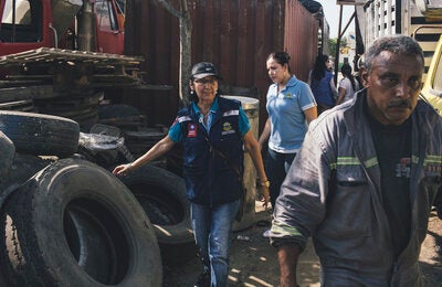 Inspection of an auto bodyshop:  In Barranquilla, initiatives such as Mi Cuadra sin Dengue — neighborhood without dengue- mobilize health workers to educate the population on how to eliminate mosquito breeding sites. The tires where rainwater collects are perfect mosquito breeding sites. Old tires are removed, while serviceable tires are placed indoors.