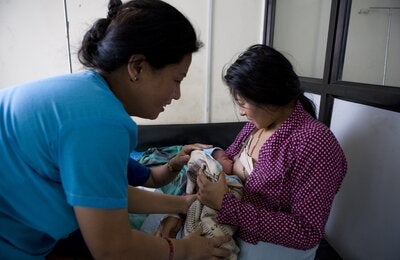 Nurse assisting a mother to breastfeed her baby