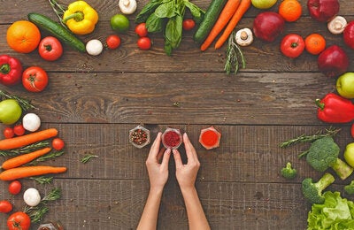 Photo of a brown table seen from above with a couple of hands holding spices recipients and framed by an array of vegetables of different colors