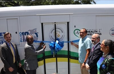 US Ambassador Mr. Nick Perry (2nd right) and Dr. the Honourable Christopher Tufton, Minister of Health and Wellness (3rd right) are ready to cut the ribbon for the newly donated mobile vaccination unit. In good spirits and smiling are (L-R) Mr. Alex Gainer, Acting Country Representative for USAID in Jamaica, Mr. Ian Stein, PAHO/WHO Representative to Jamaica, Bermuda and the Cayman Islands and Dr. Marion Bullock DuCasse, Advisor for Health Emergencies at PAHO.