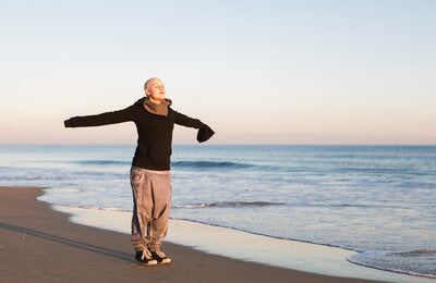 Bald woman with her arms extended in cross, breathing in in a beach.
