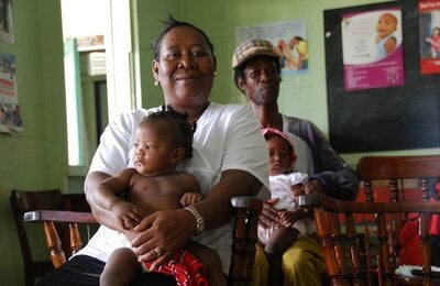 Mujer sentada con bebé y, más atrás, hombre con bebé