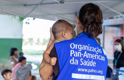 PAHO consultant holds indigenous child in their arms.