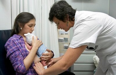 Madre con bebé en el pecho y enfermera ayudando