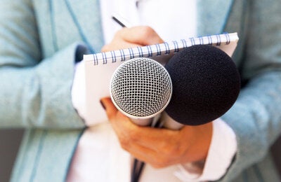 Female journalist holding a microphone and notebook.
