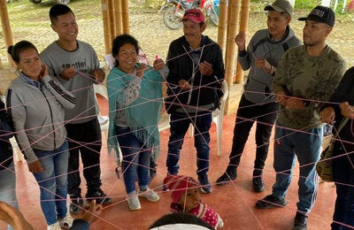 Indigenous people forming a circle and grabing a thin red interconected rope