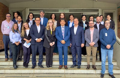 Participantes del evento (hombres y mujeres) con ropa ejecutiva, posan en las escaleras de la entrada de un edificio.