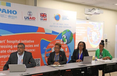 Event panelists seated. Event banner behind them.