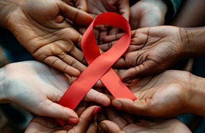 manos de personas de distintas nacionalidades sosteniendo el lazo representativo al Sida