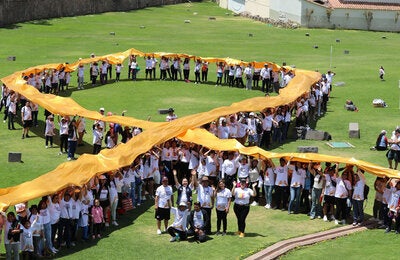 Personas en un campo amplio sosteniendo el emblema del cáncer infantil (lazo dorado)