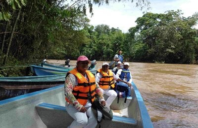 Personas en un bote de madera en la orilla de un río. Las personas tienen chalecos salvavidas.