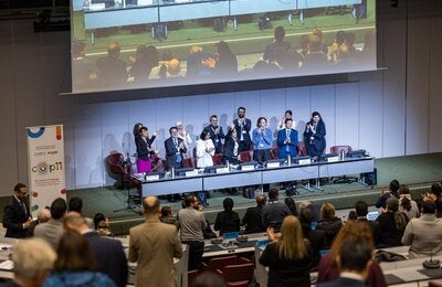 Conference room at COP11 meeting; panelists stand and applaud at the front, audience members also standing and clapping.