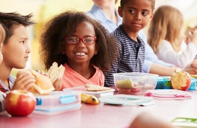 School children eating apples, bananas, and sandwiches together.
