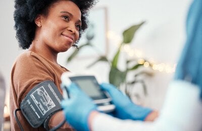 Personal de salud toma la presión arterial con un dispositivo automático a una mujer joven afrodescencdiente