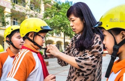 Female adult buckles helmet onto boy's head