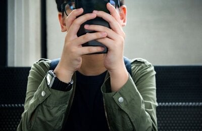 A kid seating on the couch using his mobile phone