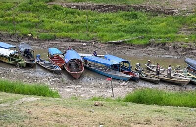 Wooden boats moored in a shallow waterway, with exposed riverbanks and low water levels visible along the channel during a period of reduced river flow in the Amazon region.