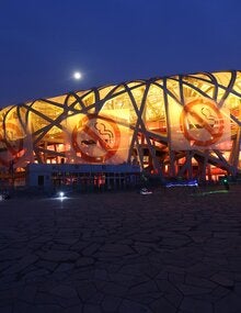 Photo of a big building shaped as a elipse, with no walls, shape made of the bent beams. In the exterior, four large banners with the icon of prohibited smoking