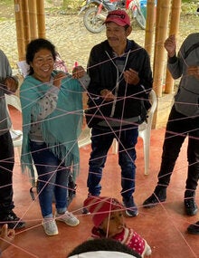 Indigenous people forming a circle and grabing a thin red interconected rope