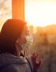 Mujer con mascarilla mirando por la ventana al atardecer