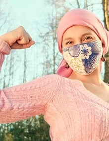 Mujer vestida de rosa con el brazo derecho levantado con el codo en ángulo recto y el puño en alto en señal de lucha. Lleva un gorro rosa y la nariz y la boca cubiertos por una mascarilla de tela