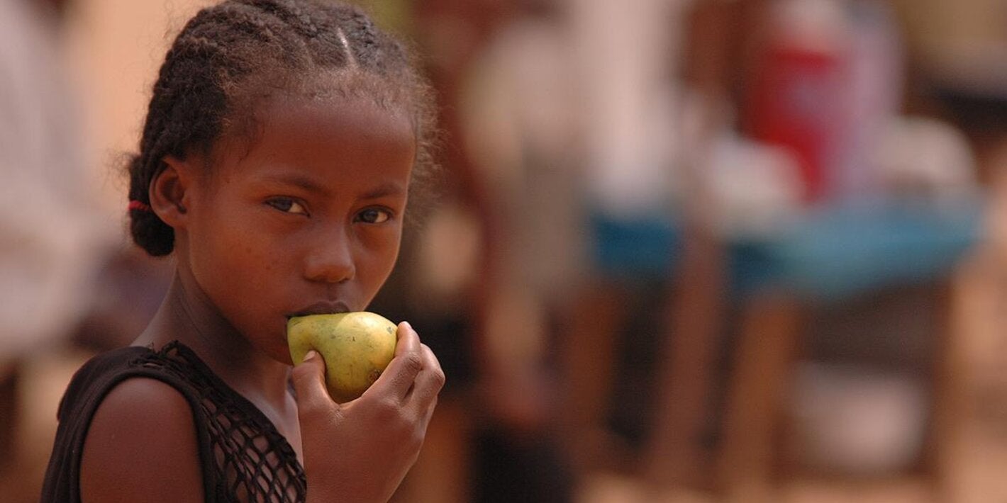 Photo of a young girl with braided hair eating a pear