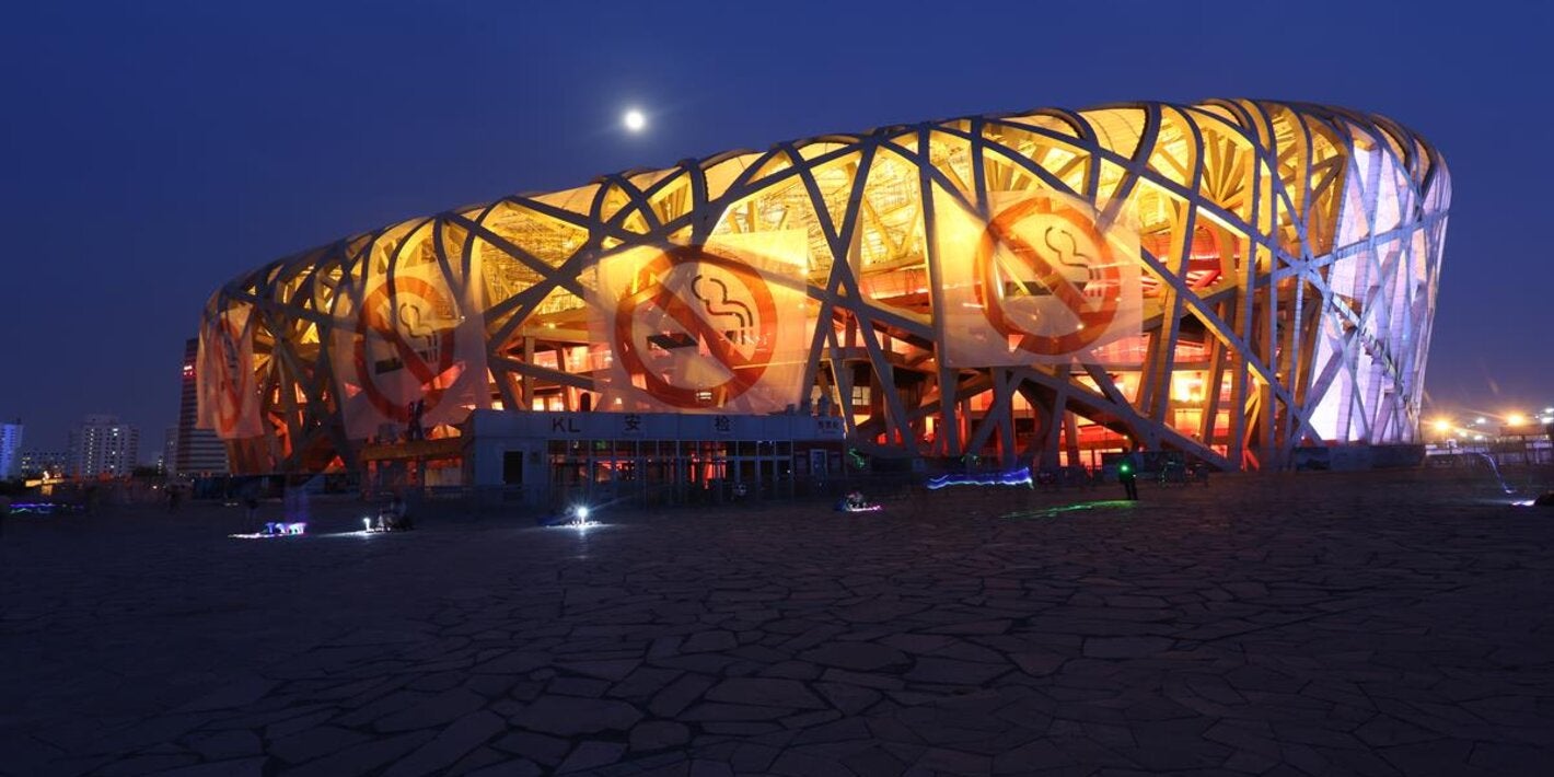 Photo of a big building shaped as a elipse, with no walls, shape made of the bent beams. In the exterior, four large banners with the icon of prohibited smoking
