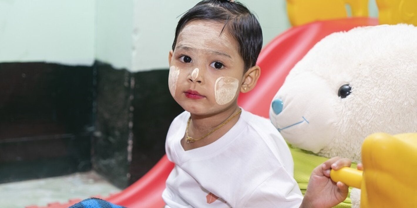 Photo of a young girl with her face painted and seated next to a giant stuffed rabitt
