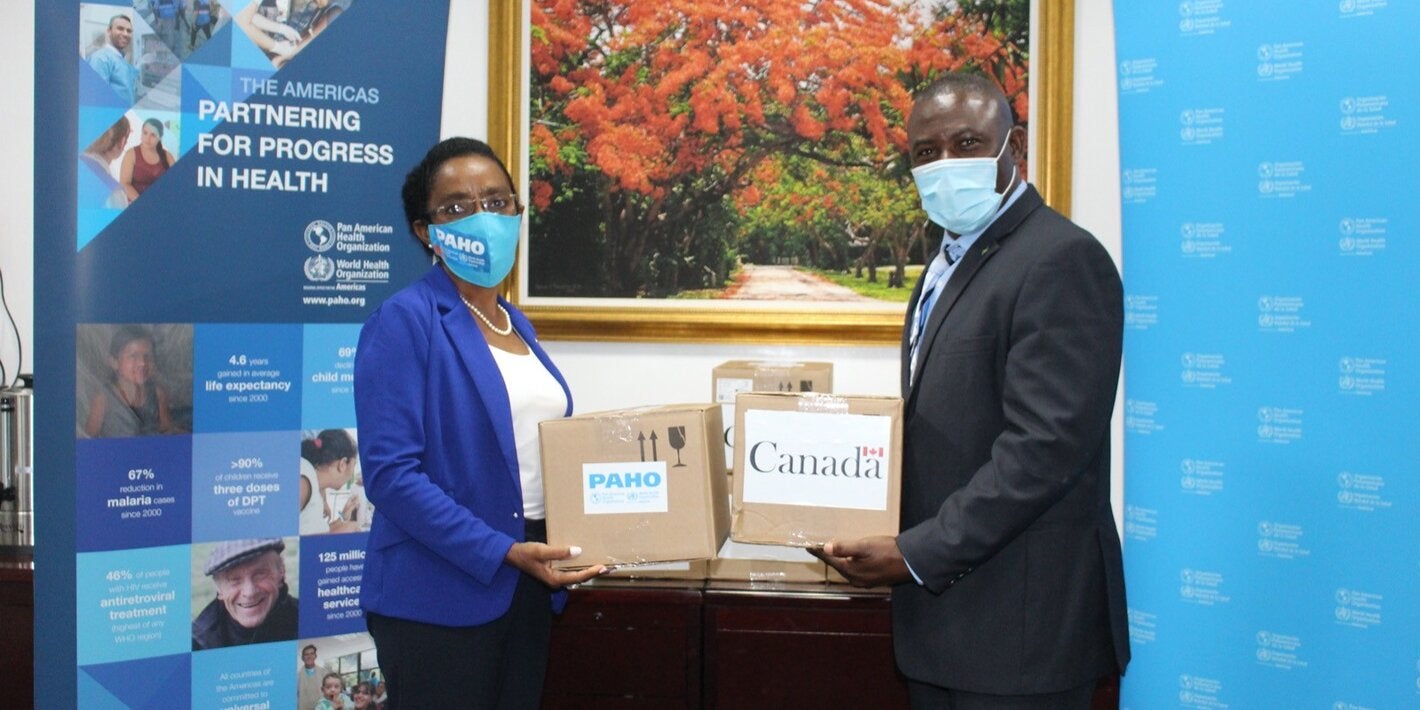 Dr Eldonna Boisson, PAHO-WHO Representative and Minister Renward Wells, Minister of Health hold donations of COVID-19 test kits 