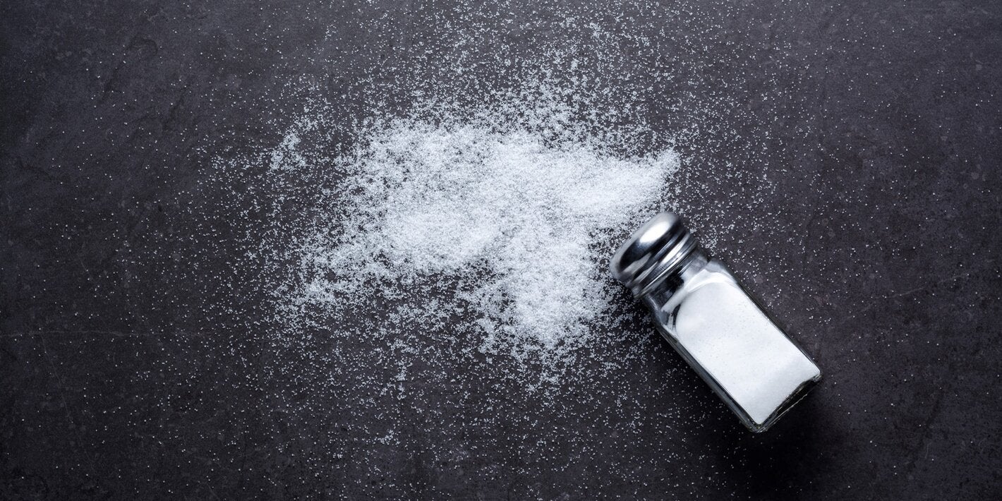 Salt shaker with salt spilt around on a dark background