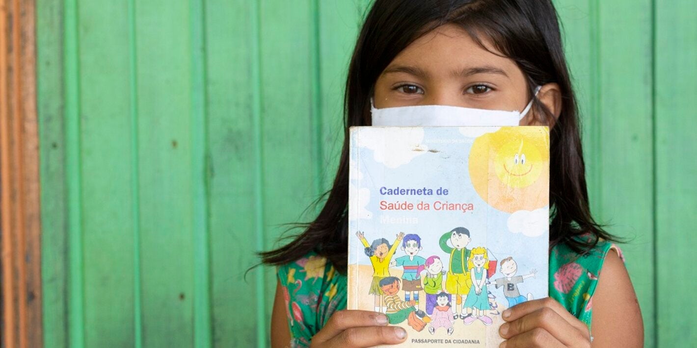 Criança segurando cartão de vacinação, no Brasil