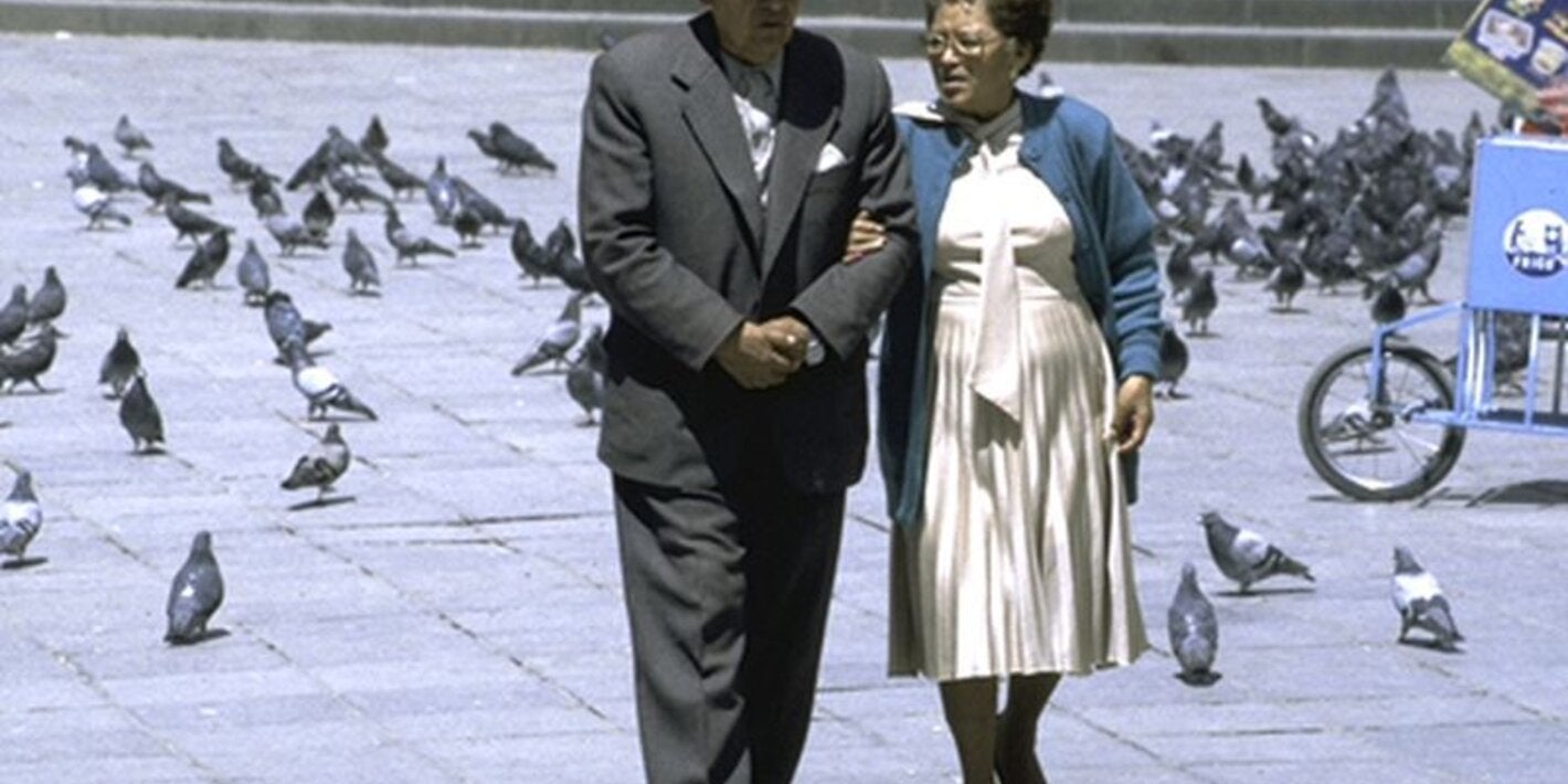 aging couple walking among pigeons in a plaza