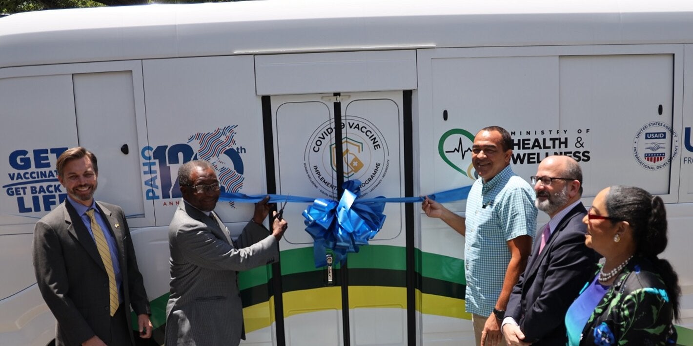 US Ambassador Mr. Nick Perry (2nd right) and Dr. the Honourable Christopher Tufton, Minister of Health and Wellness (3rd right) are ready to cut the ribbon for the newly donated mobile vaccination unit. In good spirits and smiling are (L-R) Mr. Alex Gainer, Acting Country Representative for USAID in Jamaica, Mr. Ian Stein, PAHO/WHO Representative to Jamaica, Bermuda and the Cayman Islands and Dr. Marion Bullock DuCasse, Advisor for Health Emergencies at PAHO.
