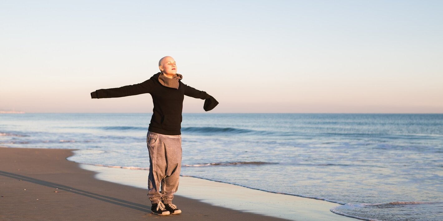 Bald woman with her arms extended in cross, breathing in in a beach.