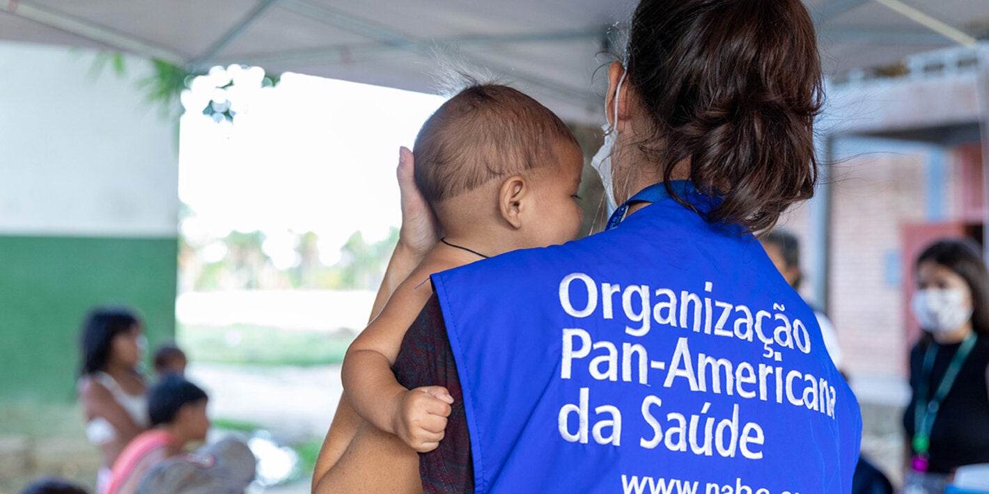 PAHO consultant holds indigenous child in their arms.
