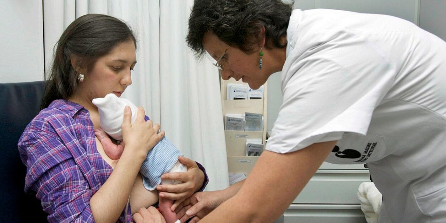 Madre con bebé en el pecho y enfermera ayudando