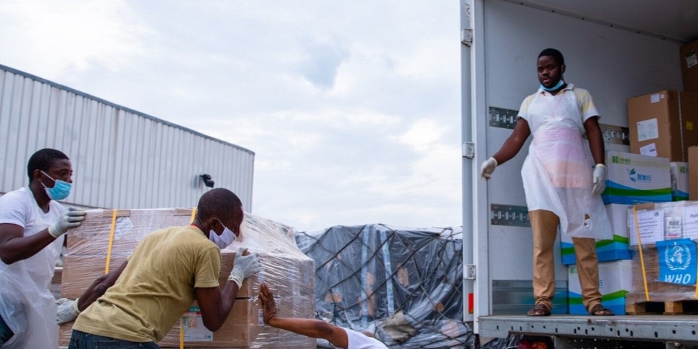 Photo of a group of workers pulling up a load of medicines marked with WHO logo into a truck