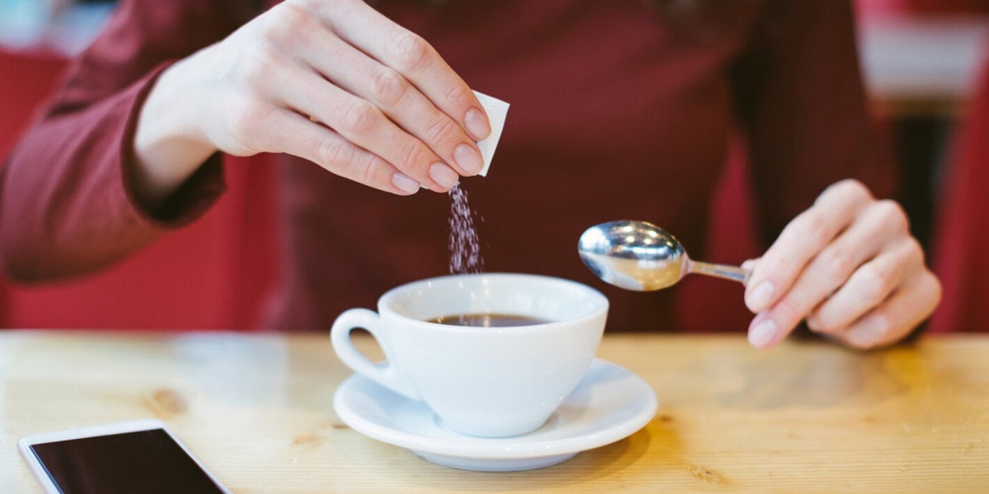 Person adding sugar to beverage. Avoid non-sugar sweeteners